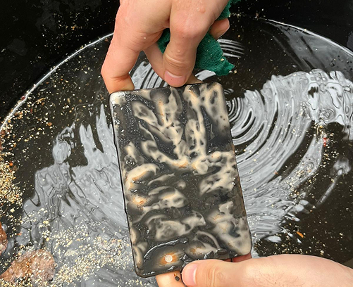 Manos de artesano bruñendo una pieza de cerámica para compactar la superficie antes de la cocción de Terra Sigillata.