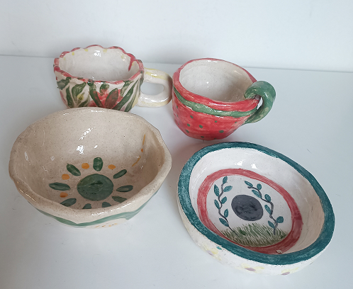 Selección de vajilla artesanal de cerámica que incluye dos tazas decoradas y dos cuencos con motivos vegetales y florales.