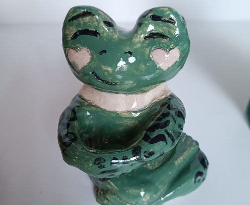 Figura de cerámica esmaltada de una rana verde sentada con detalles de corazones en las mejillas y acabado brillante.