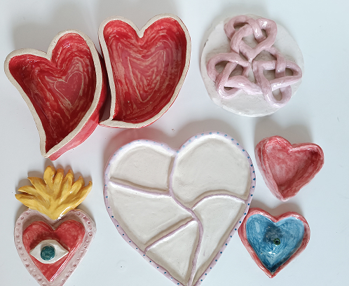 Colección de piezas de cerámica con temática de corazones, incluyendo cuencos rojos, un plato dividido blanco y un corazón decorativo con un ojo central.