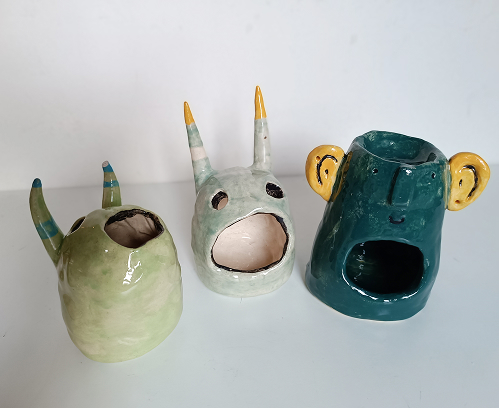 Tres portavelas de cerámica con formas de monstruos divertidos y originales en tonos verde claro y turquesa.