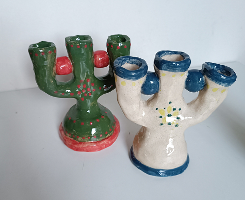 Dos candelabros de cerámica de tres brazos, uno de color verde con puntos rojos y otro blanco con detalles azules y amarillos.