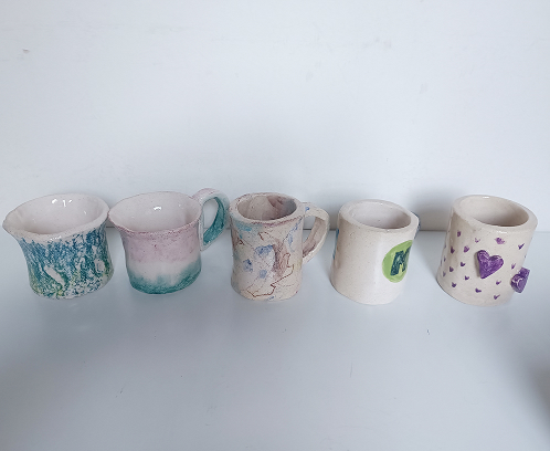 Conjunto de cinco tazas de cerámica artesanales con variados estilos de pintura y texturas en tonos pastel.