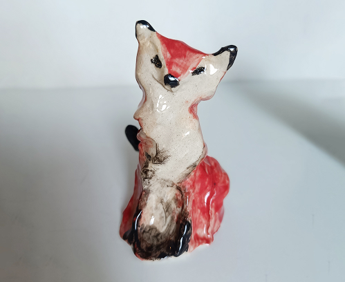 Primer plano de una figura de zorro en cerámica con acabado brillante, pintado en colores blanco, rojo y negro.
