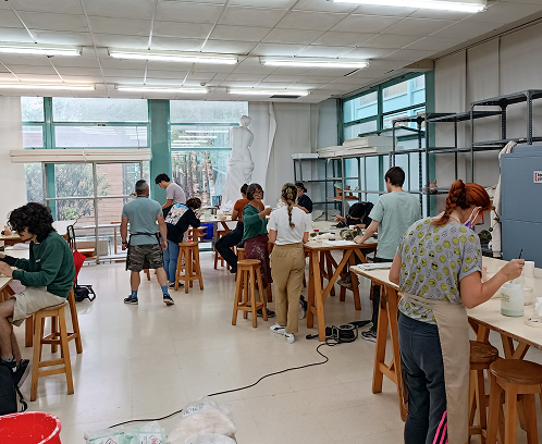 Primer plano de manos expertas modelando una pieza circular de arcilla sobre una mesa de madera durante el taller de Raku.