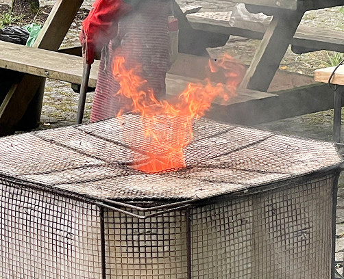 Vista detallada de las pinzas metálicas sujetando una pieza de cerámica incandescente recién extraída del horno de gas.
