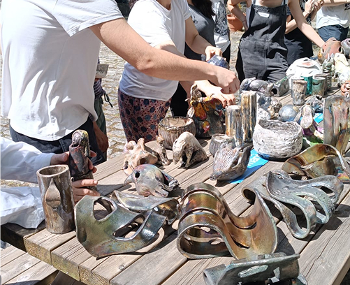 Participantes del taller observando de cerca el proceso de reducción química mientras las piezas humean dentro de los cubos de viruta de madera.