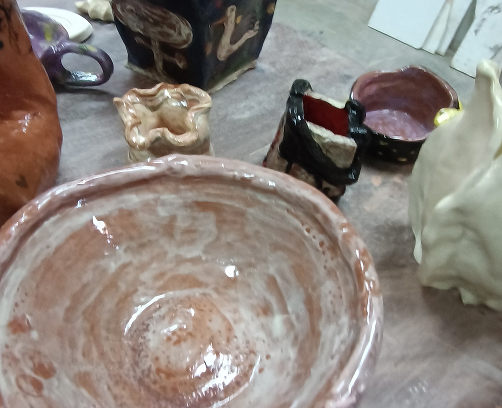 Primer plano de un cuenco de cerámica rústica con esmalte transparente que deja ver el color natural de la arcilla, junto a otras creaciones experimentales.