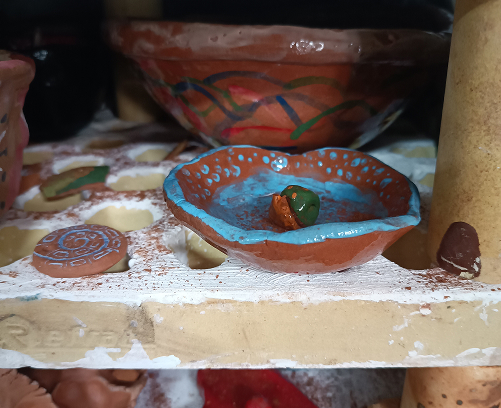 Pequeño cuenco de barro con interior esmaltado en azul turquesa y una pequeña figura decorativa en el centro, apoyado sobre una placa de horneado.