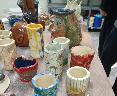 Conjunto de vasos y cilindros de cerámica hechos a mano, decorados con diversas técnicas: desde ilustraciones lineales de personajes hasta patrones abstractos y paisajes urbanos.