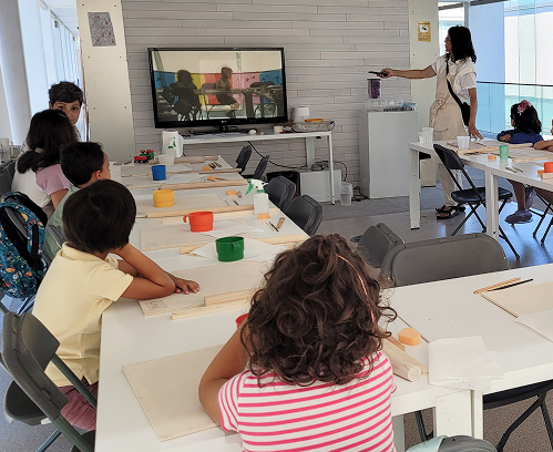 Ambiente de aprendizaje en el taller infantil de cerámica, con niños modelando piezas de barro inspiradas en la historia.