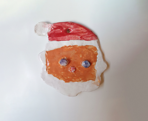 Detalle de un adorno de cerámica de Papá Noel con rostro anaranjado, ojos azules en relieve y gorro rojo clásico.