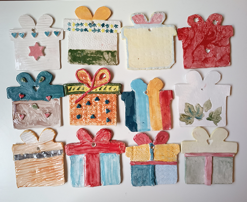 Variedad de adornos de cerámica con forma de cajas de regalo, decorados con lazos de colores, texturas de estrellas y patrones geométricos.