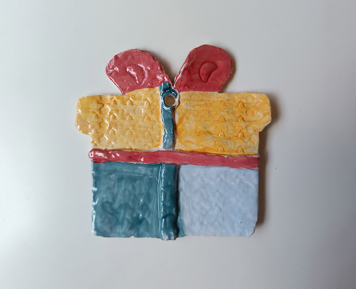 Figura de cerámica de un regalo navideño con textura de estrellas amarillas, lazo rojo y base dividida en azul y blanco.