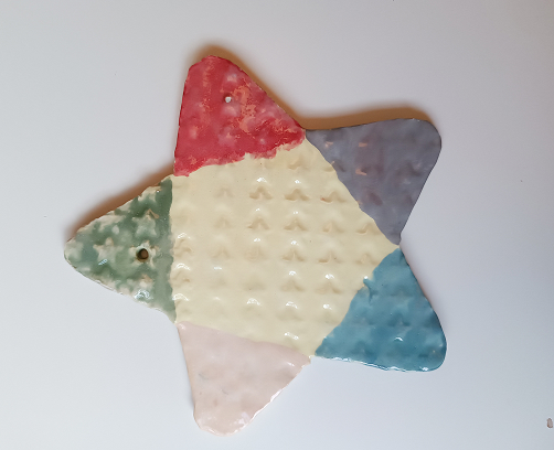 Figura de cerámica de un regalo navideño con textura de estrellas amarillas, lazo rojo y base dividida en azul y blanco