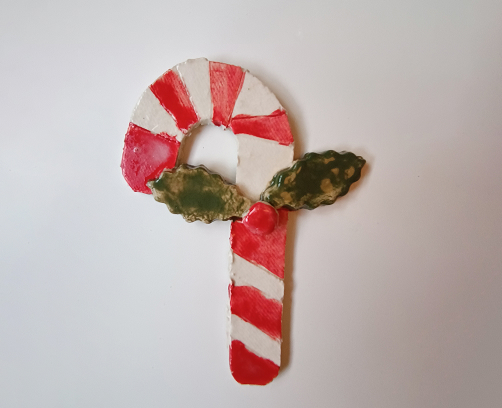 Adorno navideño de cerámica en forma de bastón de caramelo con rayas rojas y blancas y detalle de hojas de acebo en relieve.