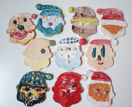 Colección de caras de Papá Noel en cerámica artesanal, cada una con expresiones únicas, barbas blancas texturizadas y gorros rojos.